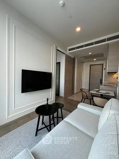Modern living room with sleek design, featuring a wall-mounted TV, stylish furniture, and open kitchen layout.