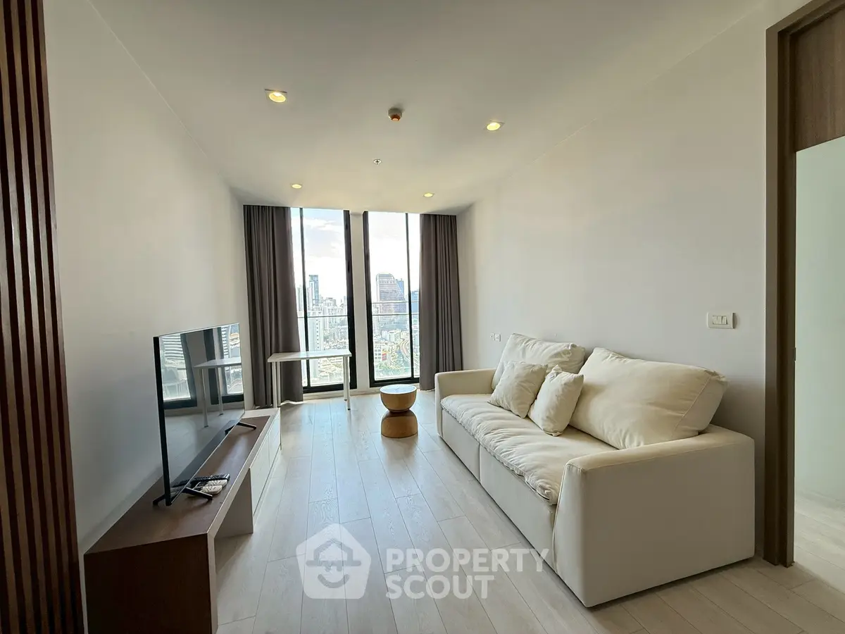 Modern living room with city view, featuring sleek furniture and floor-to-ceiling windows.