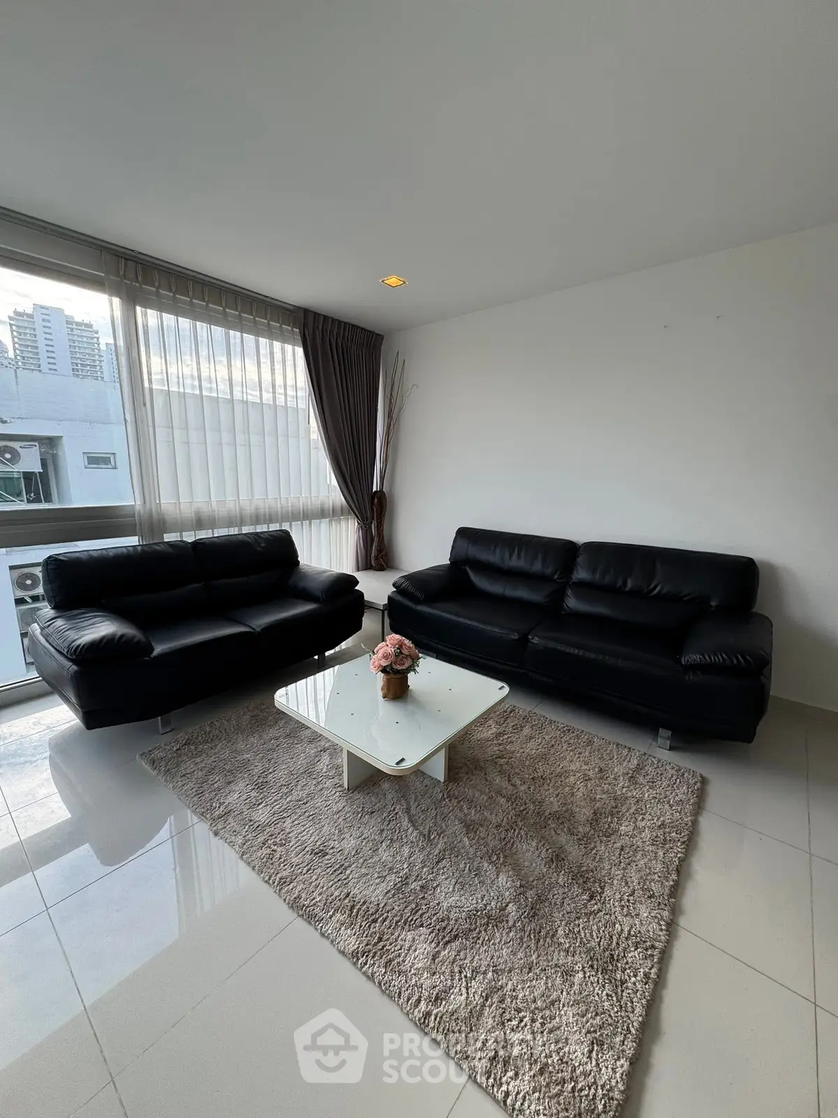 Modern living room with black leather sofas and glass coffee table in bright apartment.