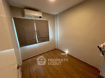Spacious empty bedroom with wooden flooring and air conditioning, ready for customization.