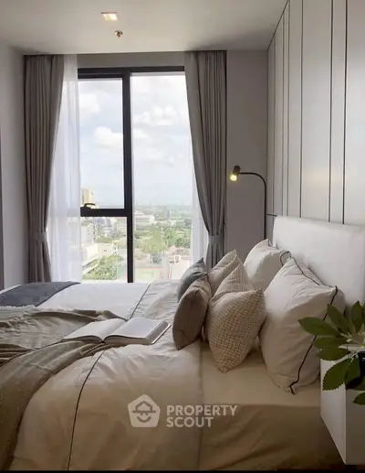 Modern bedroom with large window offering stunning city view, elegant decor, and cozy bedding.