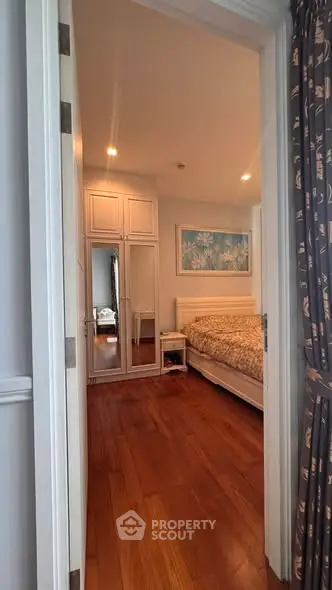 Elegant bedroom with wooden flooring and mirrored wardrobe, perfect for cozy living.