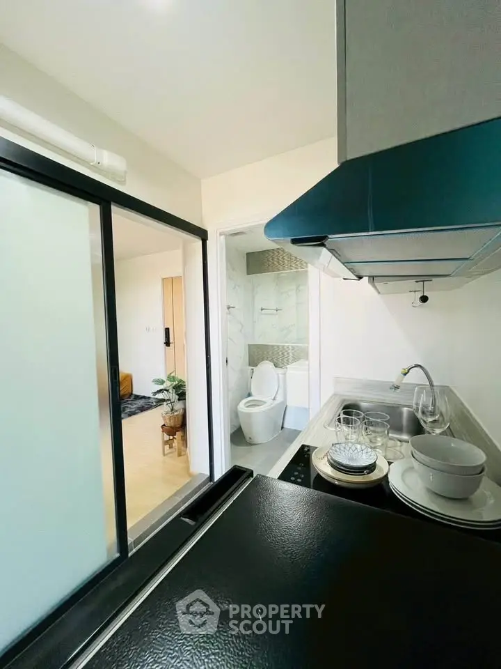 Modern kitchen with sliding door and view into bathroom, featuring sleek appliances and minimalist design.