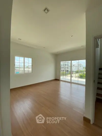 Spacious unfurnished living room with large windows and wooden flooring, perfect for customization.