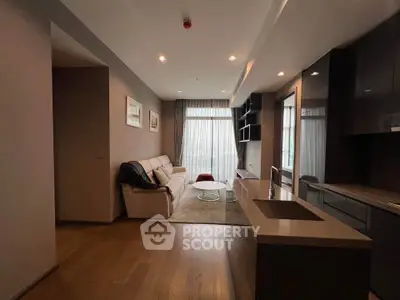 Modern living room with open kitchen, featuring sleek design and natural light from large windows.