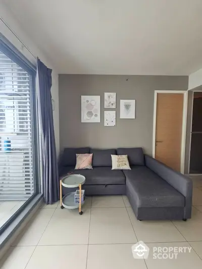 Modern living room with stylish gray sofa and wall art, featuring large windows for natural light.