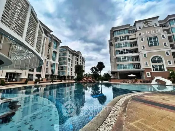 Luxurious residential complex with stunning pool and modern architecture under cloudy sky.
