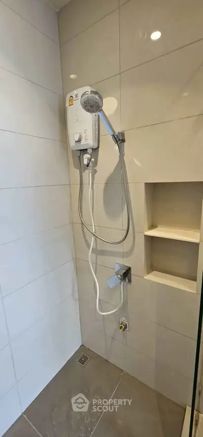 Modern bathroom shower area with sleek tiles and built-in shelving.