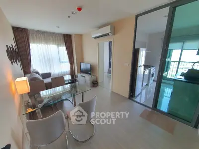 Modern living room with glass dining table and view into kitchen with washing machine.