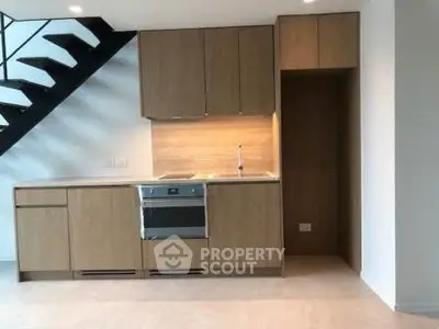 Modern kitchen with sleek wooden cabinetry and built-in oven under a stylish staircase.