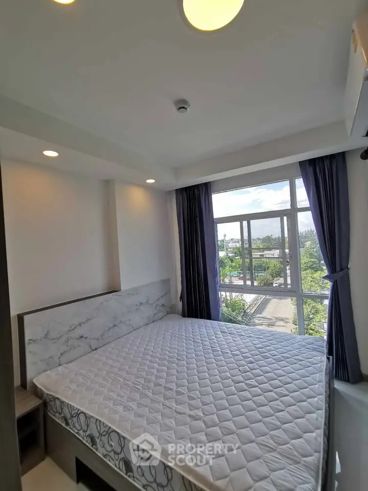 Bright and airy bedroom with large window and modern decor in a high-rise apartment.