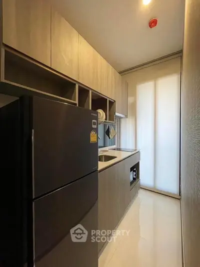 Modern kitchen with sleek cabinetry and black refrigerator in compact layout.