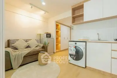 Modern living room with integrated kitchen and washing machine, featuring cozy sofa and stylish decor.