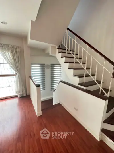 Elegant staircase with wooden flooring and modern window treatments in a bright interior space.