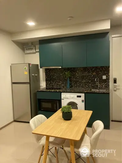 Modern kitchen with teal cabinets, washing machine, and dining set