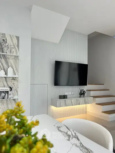 Modern living room with stylish decor and wall-mounted TV, featuring elegant marble accents and staircase.