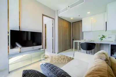 Modern living room with sleek TV setup and stylish kitchen area in open layout apartment.