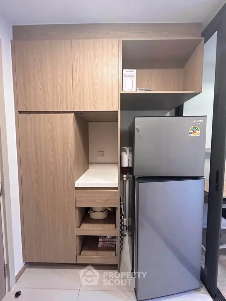 Modern kitchen with sleek wooden cabinetry and stainless steel fridge in a compact layout.