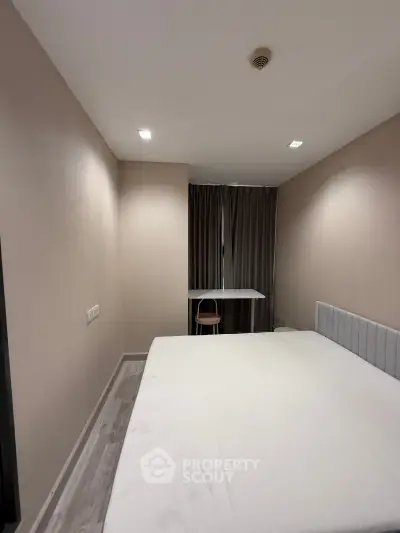 Modern minimalist bedroom with sleek design and neutral tones, featuring a comfortable bed and a small study area.