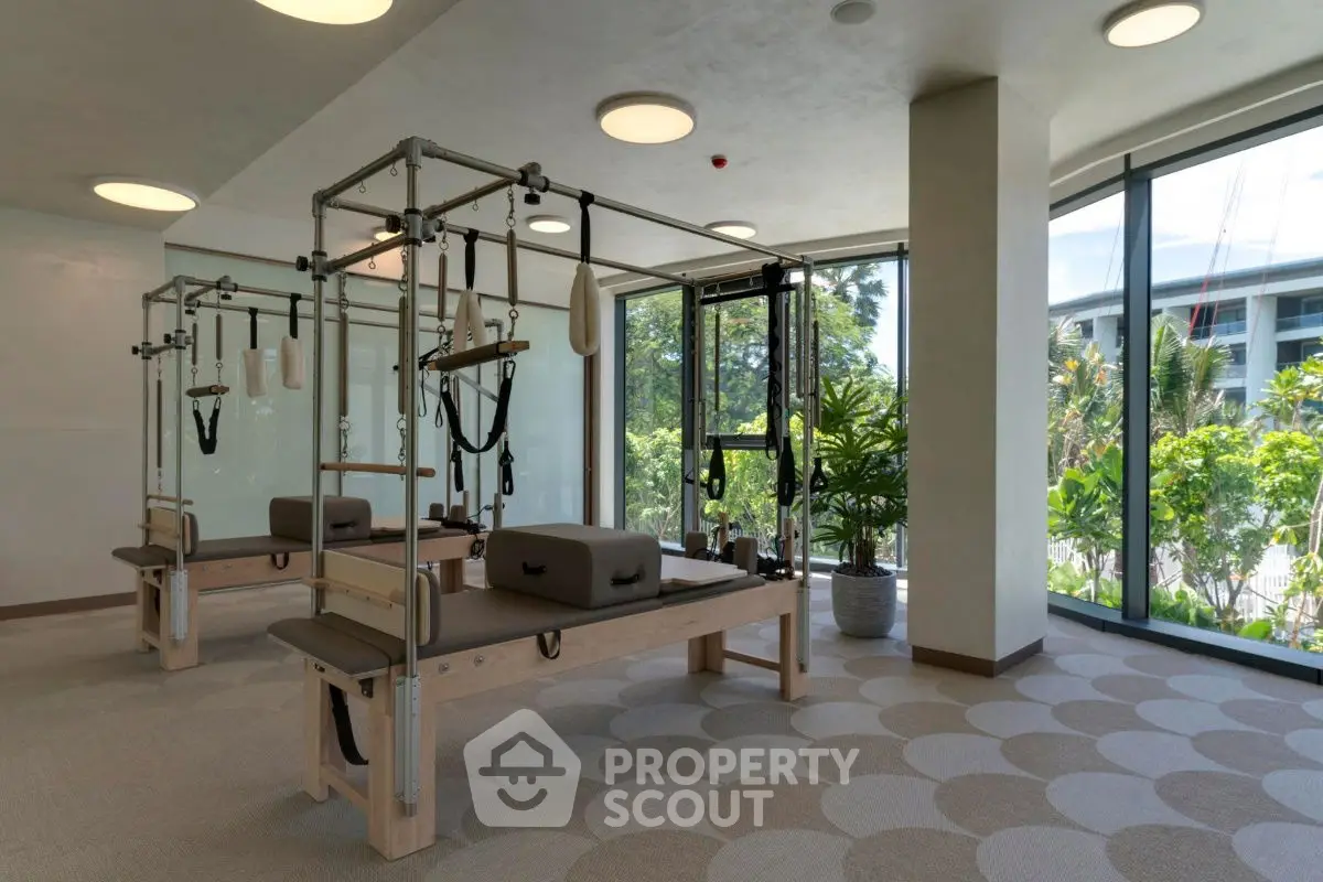 Modern gym with pilates equipment and large windows overlooking lush greenery.