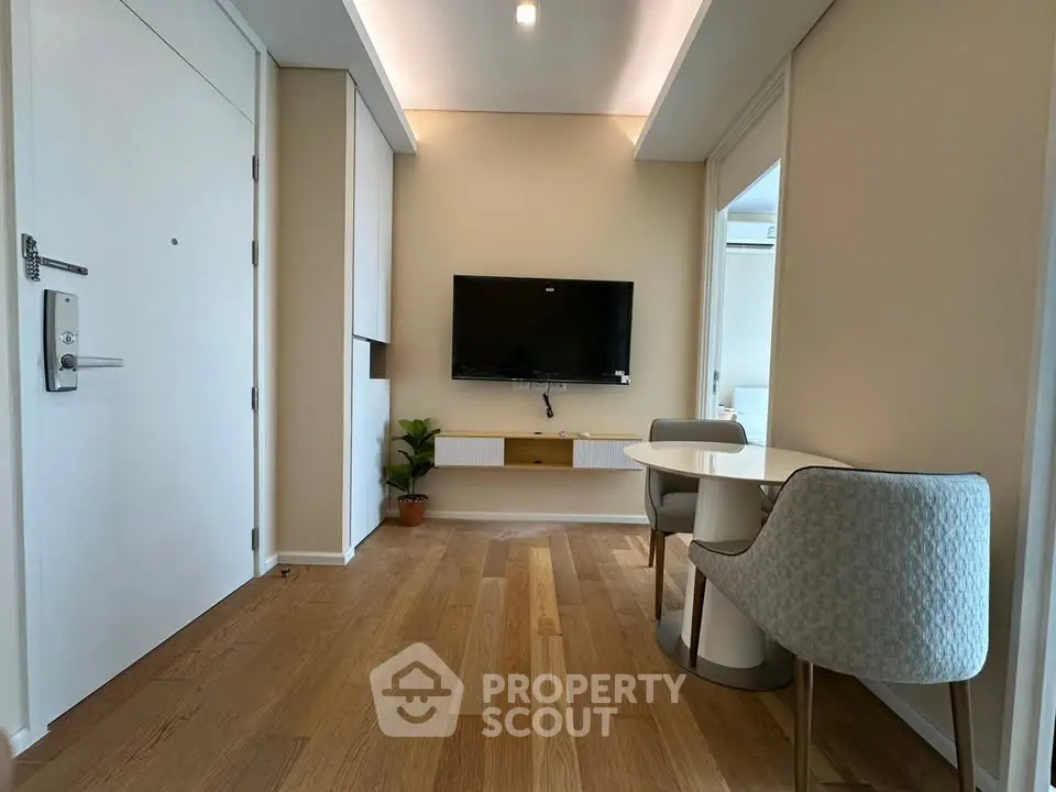 Modern living room with wooden flooring, wall-mounted TV, and cozy dining area in a stylish apartment.