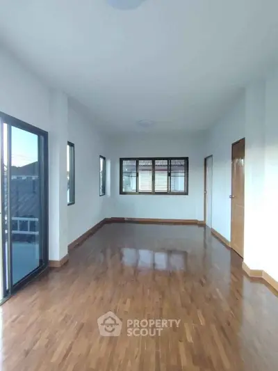 Spacious empty room with wooden flooring and large windows for natural light