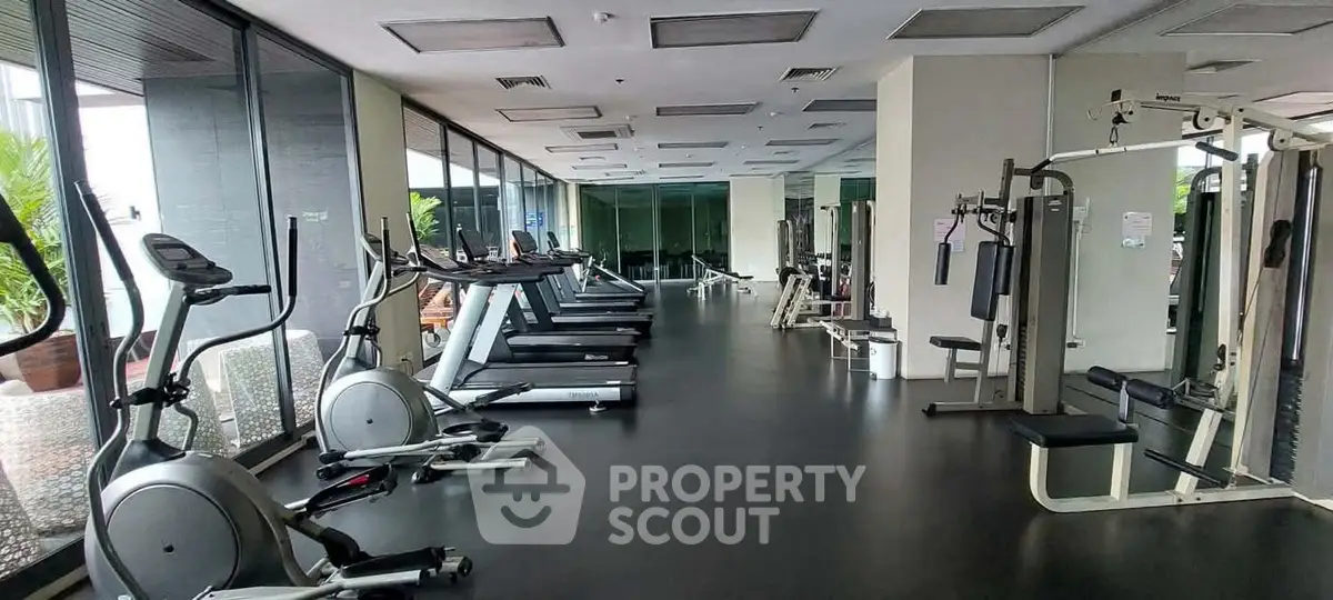 Spacious modern gym with state-of-the-art fitness equipment and large windows for natural light.