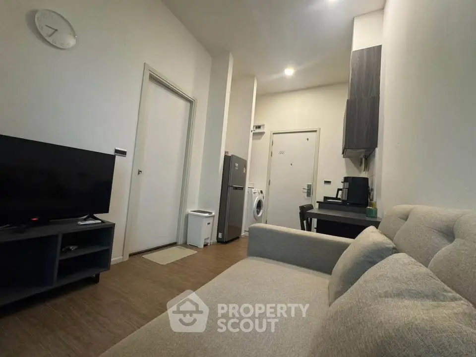 Modern living room with cozy sofa, TV, and compact kitchen appliances.