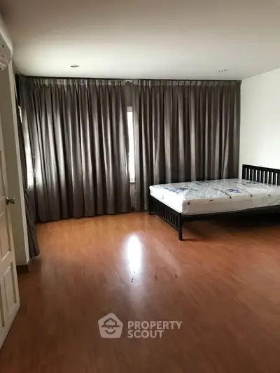 Spacious bedroom with wooden flooring and large windows for natural light.