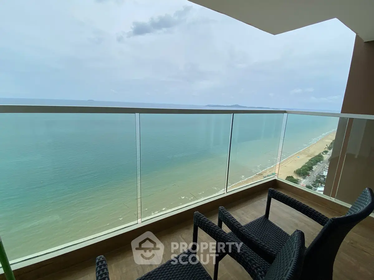 Stunning ocean view from a modern balcony with glass railing and cozy seating.