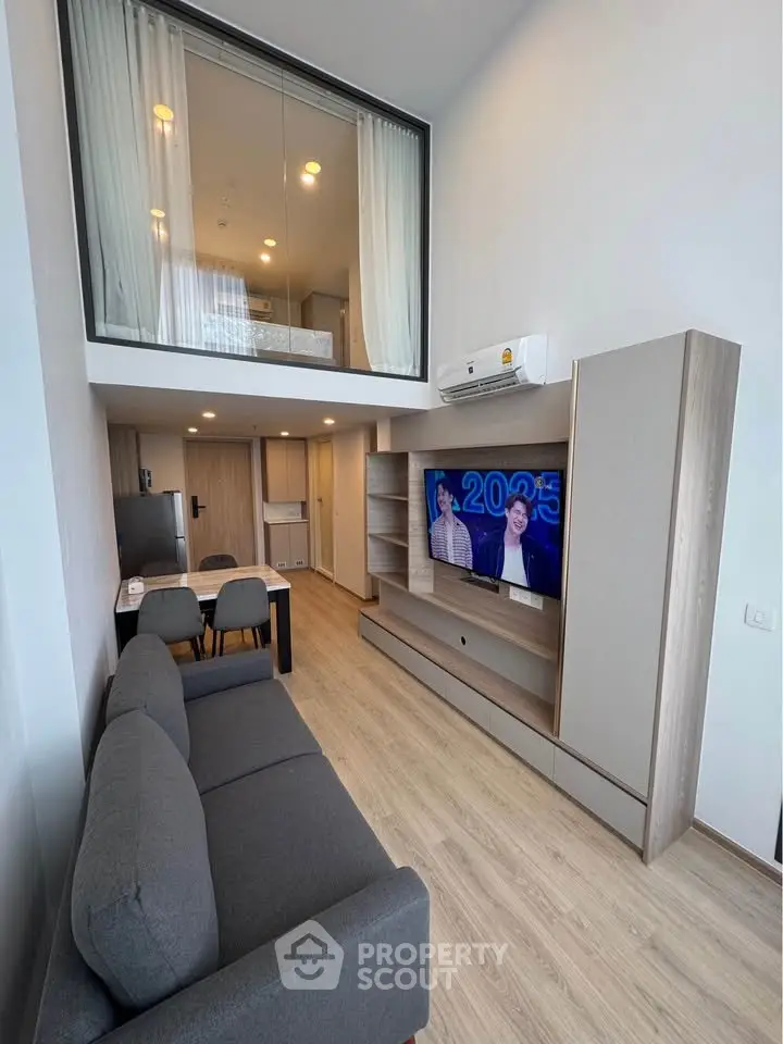 Modern loft-style living room with high ceiling and mezzanine bedroom, featuring sleek furniture and contemporary design.