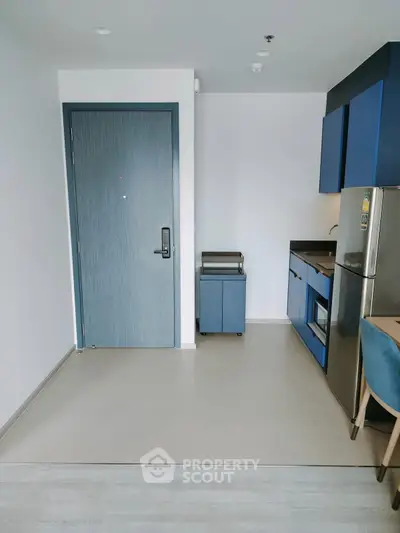Modern apartment entrance with sleek kitchen and stylish blue cabinetry.