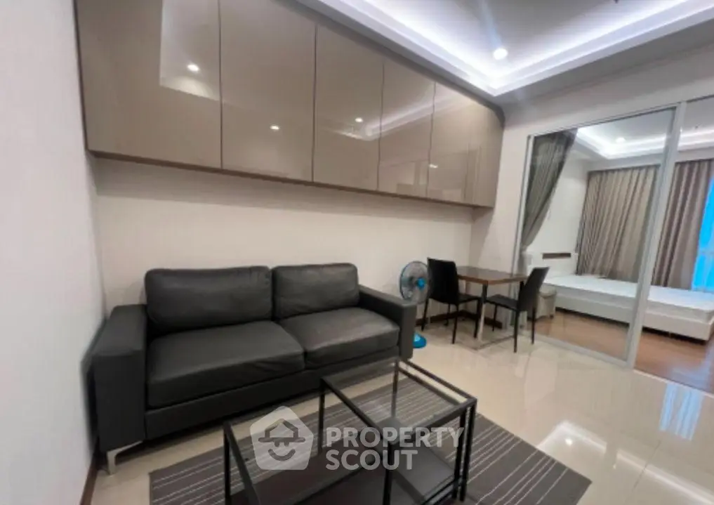 Modern living room with sleek furniture and glass partition leading to bedroom