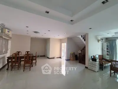 Spacious open-plan living room with dining area and staircase, featuring modern furniture and ample natural light.