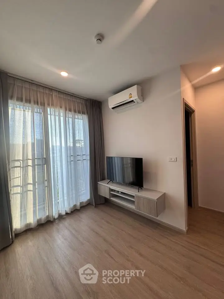Modern living room with wooden flooring, air conditioning, and natural light from large windows.