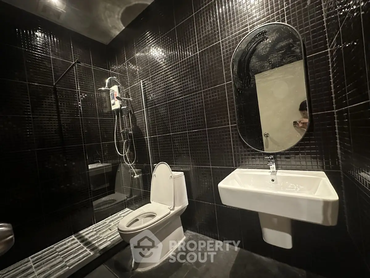 Modern black-tiled bathroom with sleek fixtures and a spacious shower area.