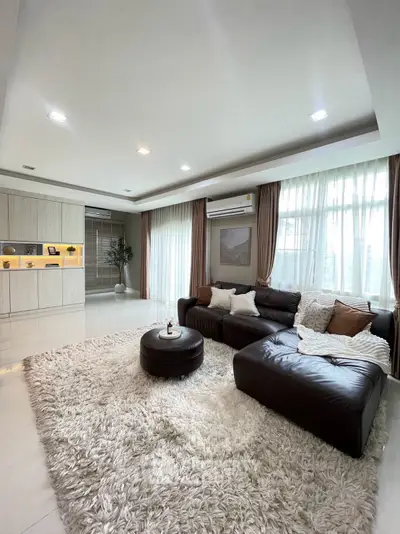 Spacious living room with plush rug and modern sectional sofa, featuring large windows and elegant decor.