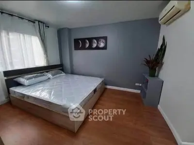 Modern bedroom with wooden flooring and moon phase artwork, featuring a comfortable bed and air conditioning.
