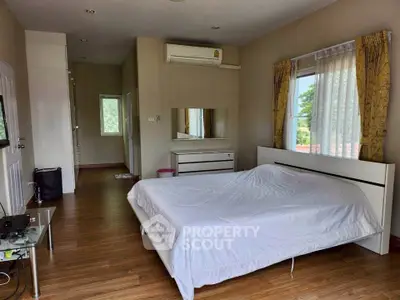 Spacious bedroom with large windows and modern furnishings, featuring a comfortable bed and wooden flooring.