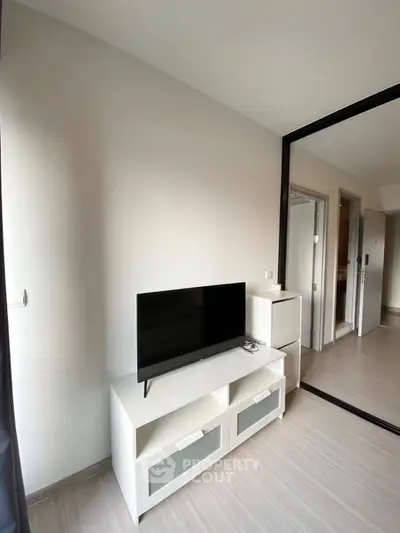 Modern living room with sleek TV stand and mirrored closet doors in a bright apartment.