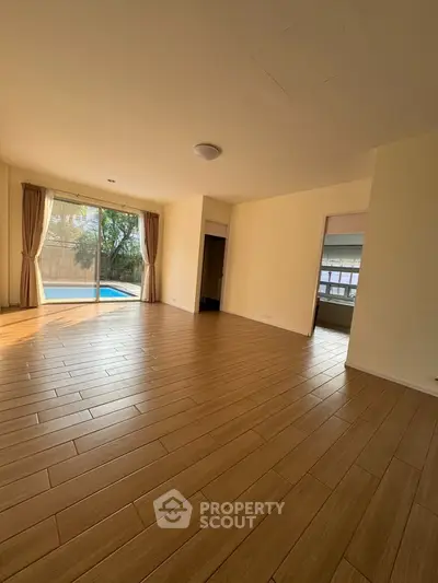 Spacious living room with wooden flooring and pool view, perfect for relaxation.