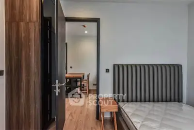 Modern bedroom with stylish headboard and wooden flooring, adjacent to a dining area.