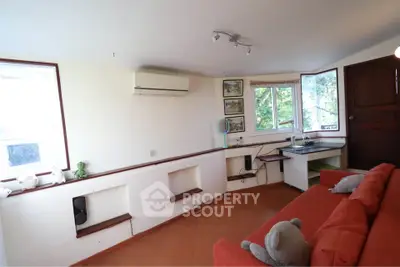 Cozy living room with red sofa, air conditioning, and large windows offering natural light and greenery views.
