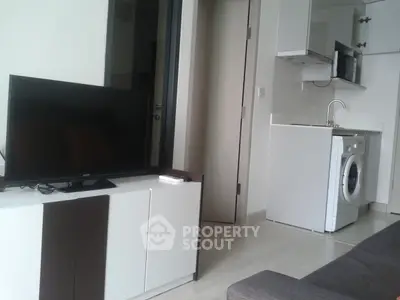 Modern compact living space with TV, washing machine, and kitchenette in a stylish apartment.