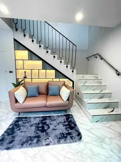 Modern living room with stylish staircase and cozy sofa, featuring elegant marble flooring and ambient lighting.