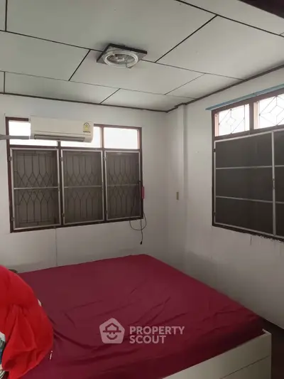 Cozy bedroom with red bedding and ample natural light from large windows.