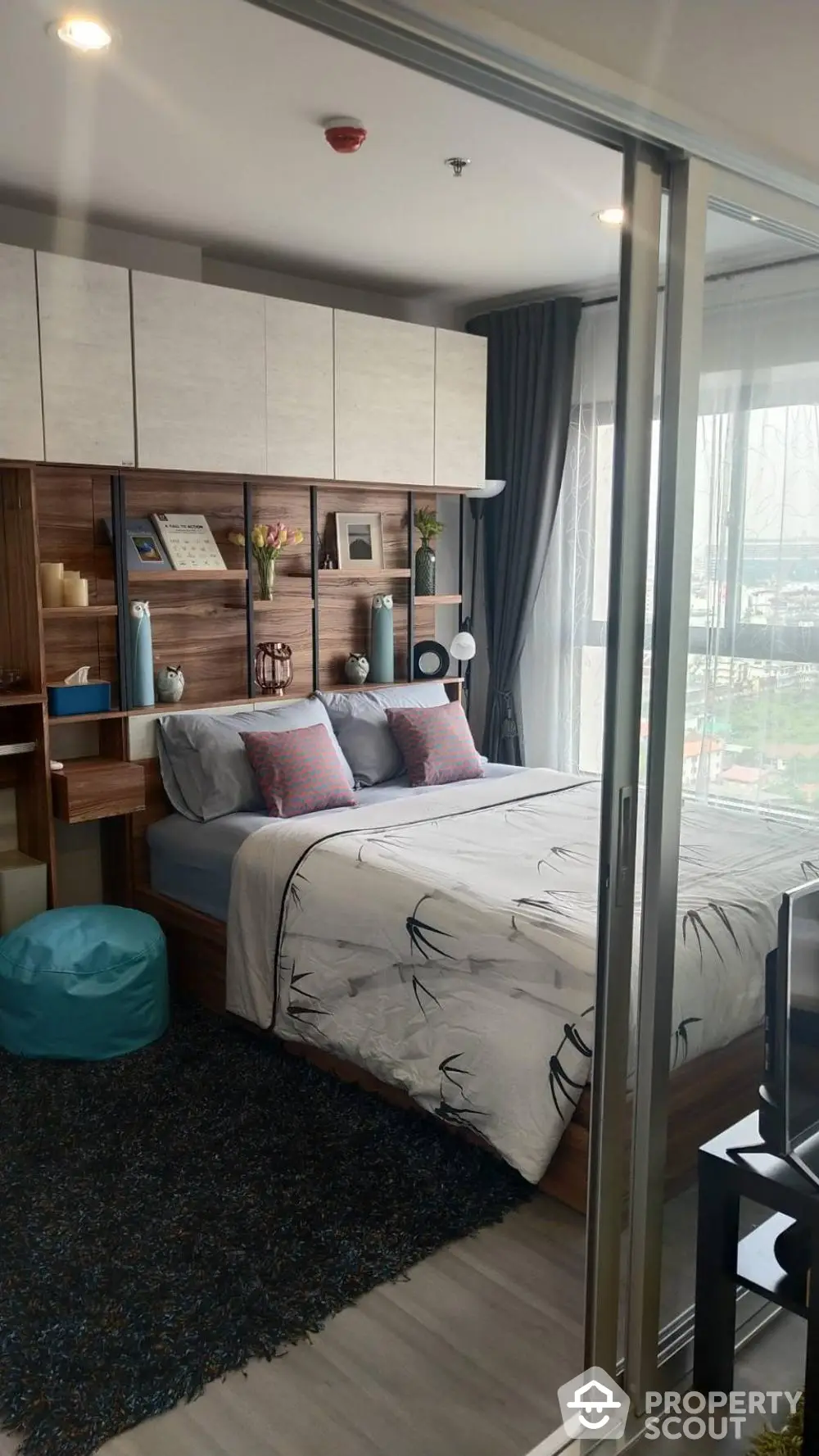 Modern bedroom with stylish decor and large window offering natural light and city view.