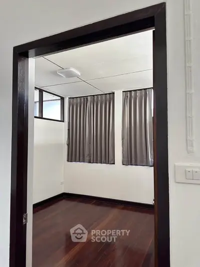 Spacious room with wooden flooring and large windows, perfect for a cozy bedroom or study.