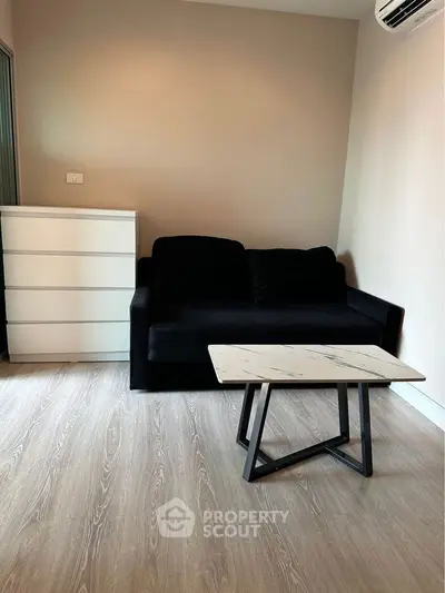 Modern living room with sleek black sofa and stylish coffee table on wooden flooring.