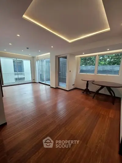 Spacious living room with wooden flooring and large windows offering natural light.